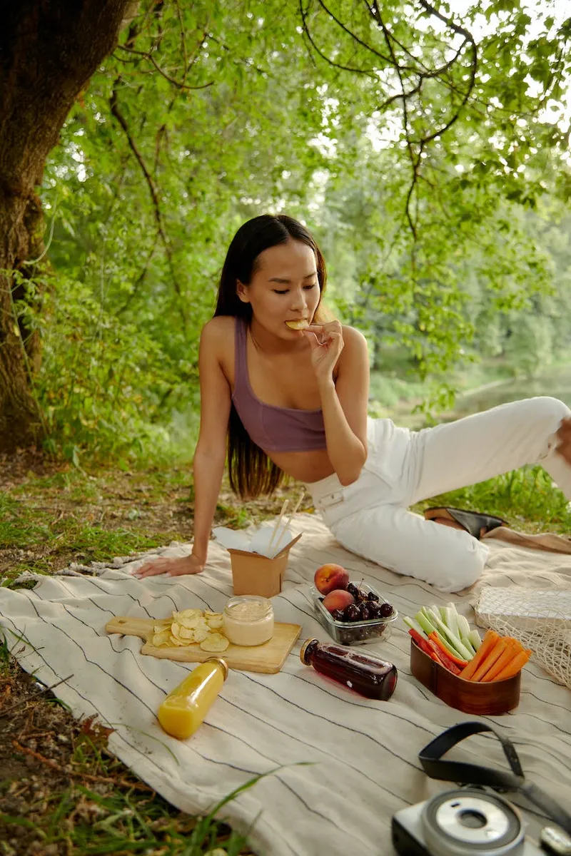 woman eating while sitting on a picnic blanket